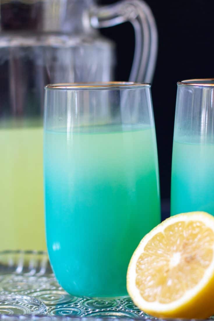 Photo of blue glasses with lemon vodka cocktail, cut lemons, and lemonade.