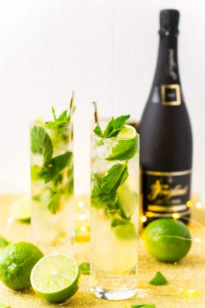 tall mojito glasses with yellow champagne, lime, basil and a black champagne bottle