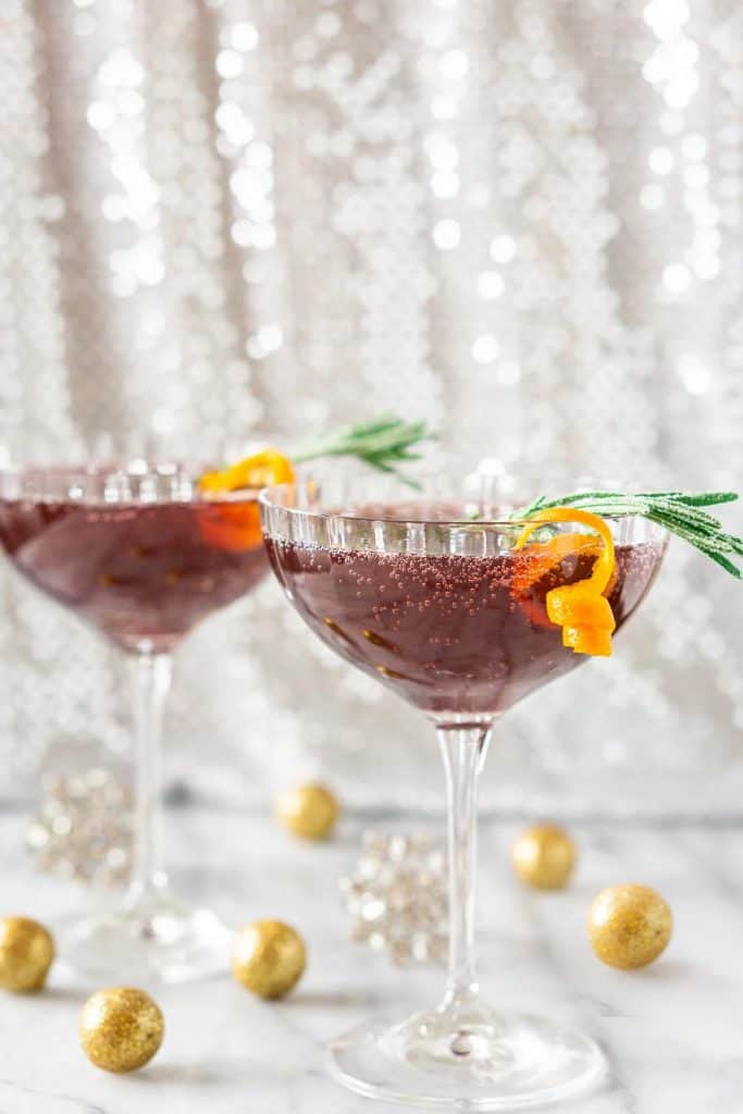 two martini glasses of dark red pomegranate with orange and green garnish